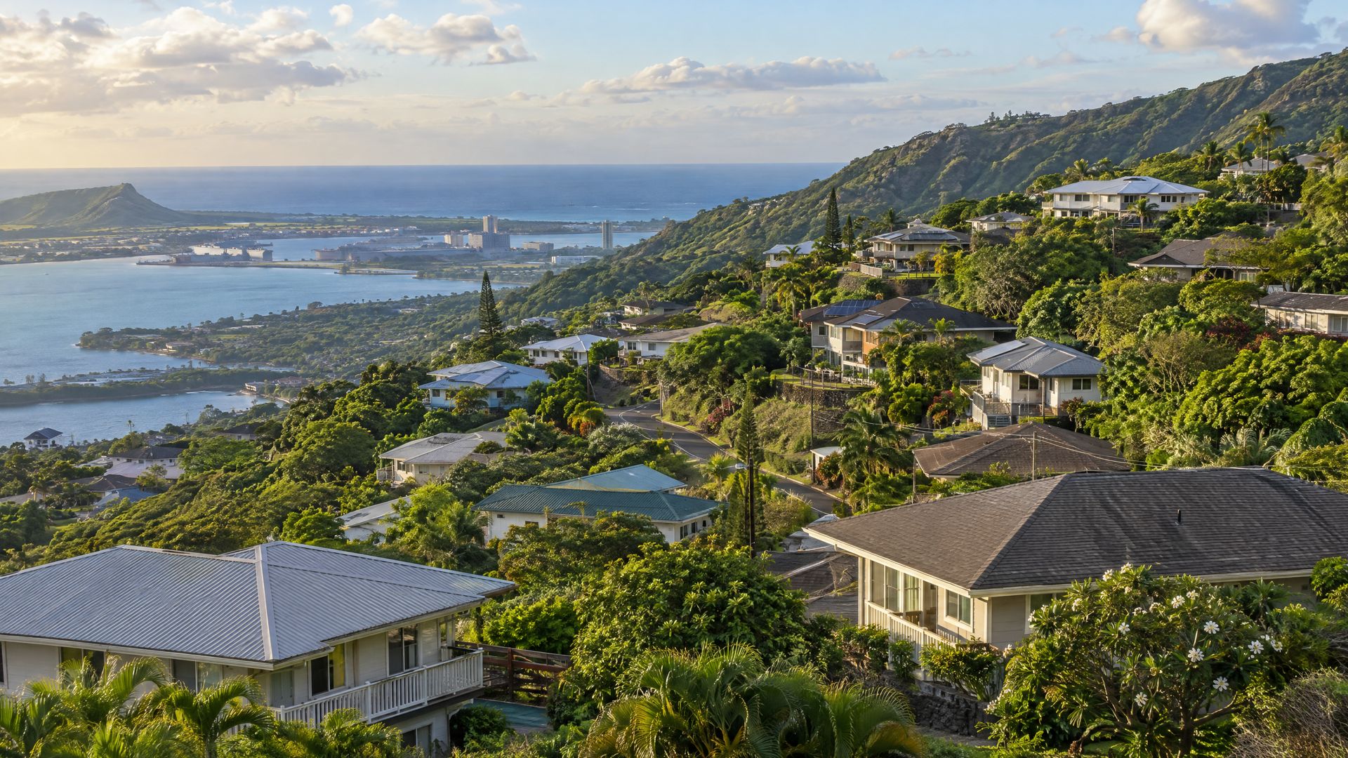 Hillside homes on green ridges in Aiea, with harbor water and the sea in the distance.