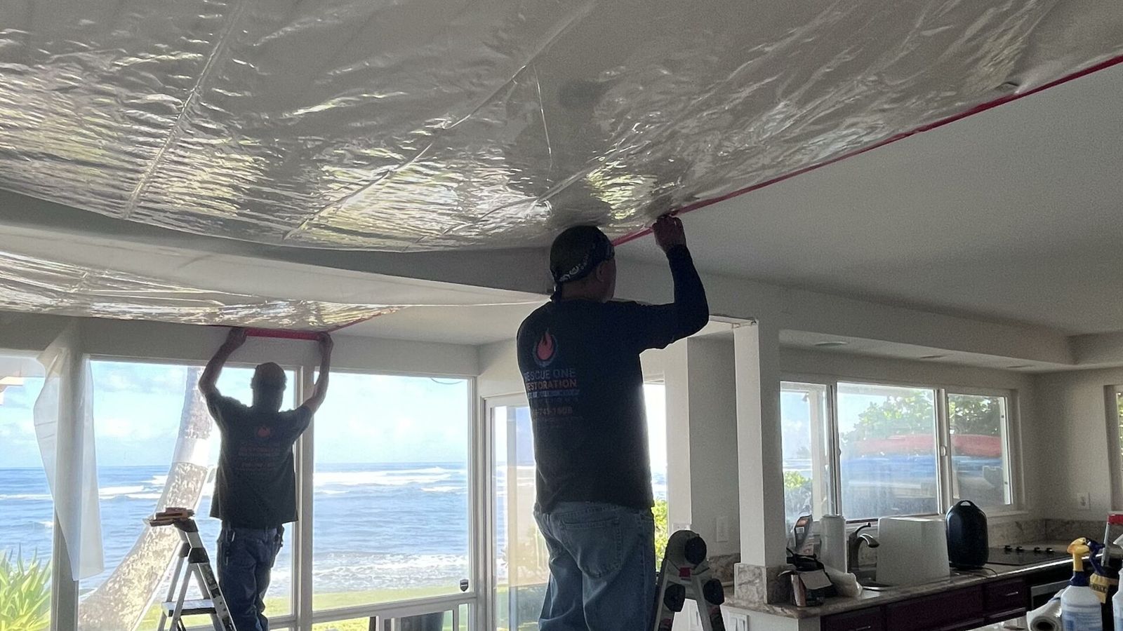 A Rescue One technician on a ladder covering a water-damaged ceiling in an oceanfront Oahu home.