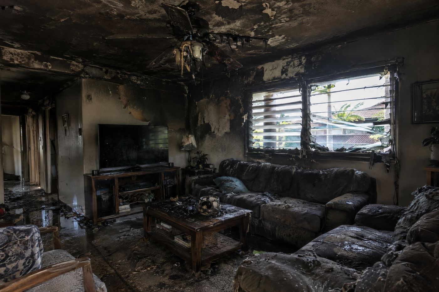 A living room in an Oahu home with a charred ceiling and heavy smoke staining after a fire.