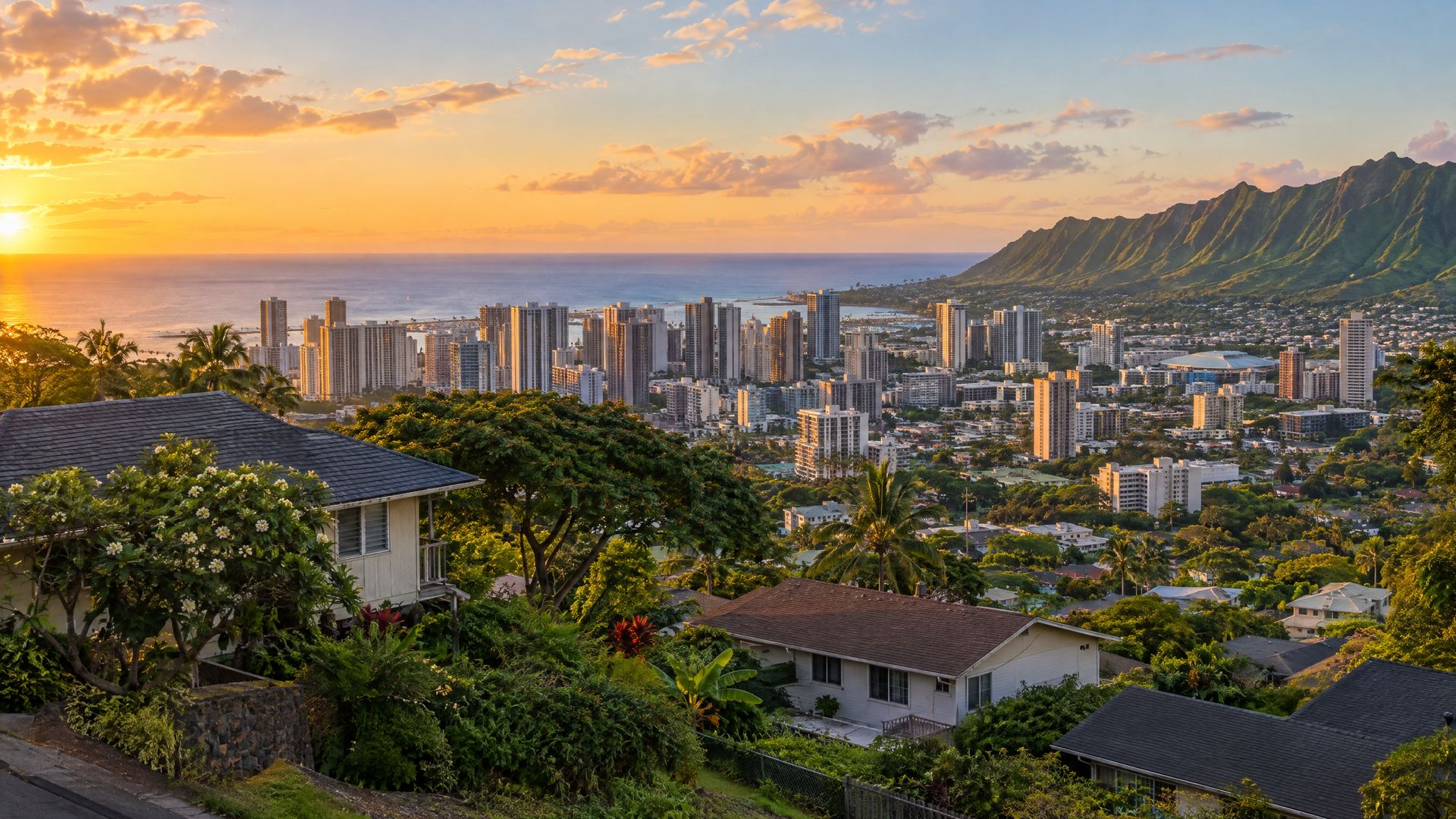 Hillside homes above Honolulu's high-rise skyline with the ocean on the horizon at sunset.