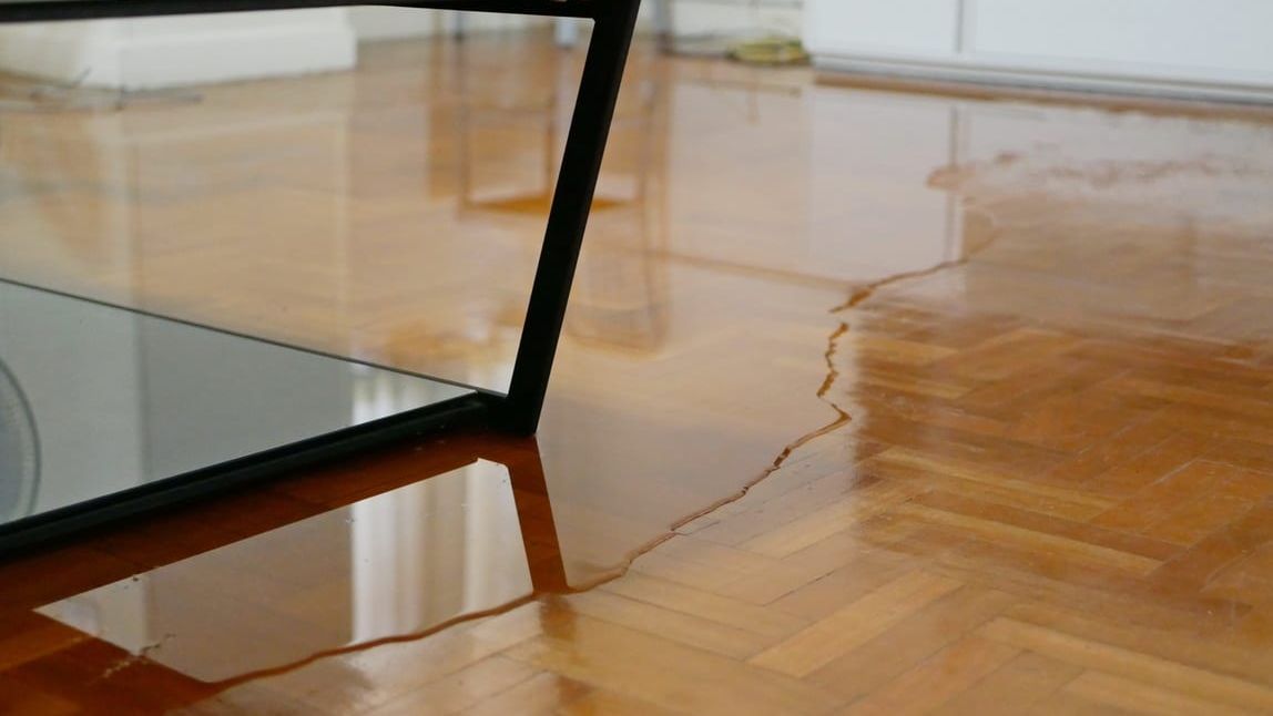 Standing water spreading across a parquet hardwood floor in a Honolulu living room.