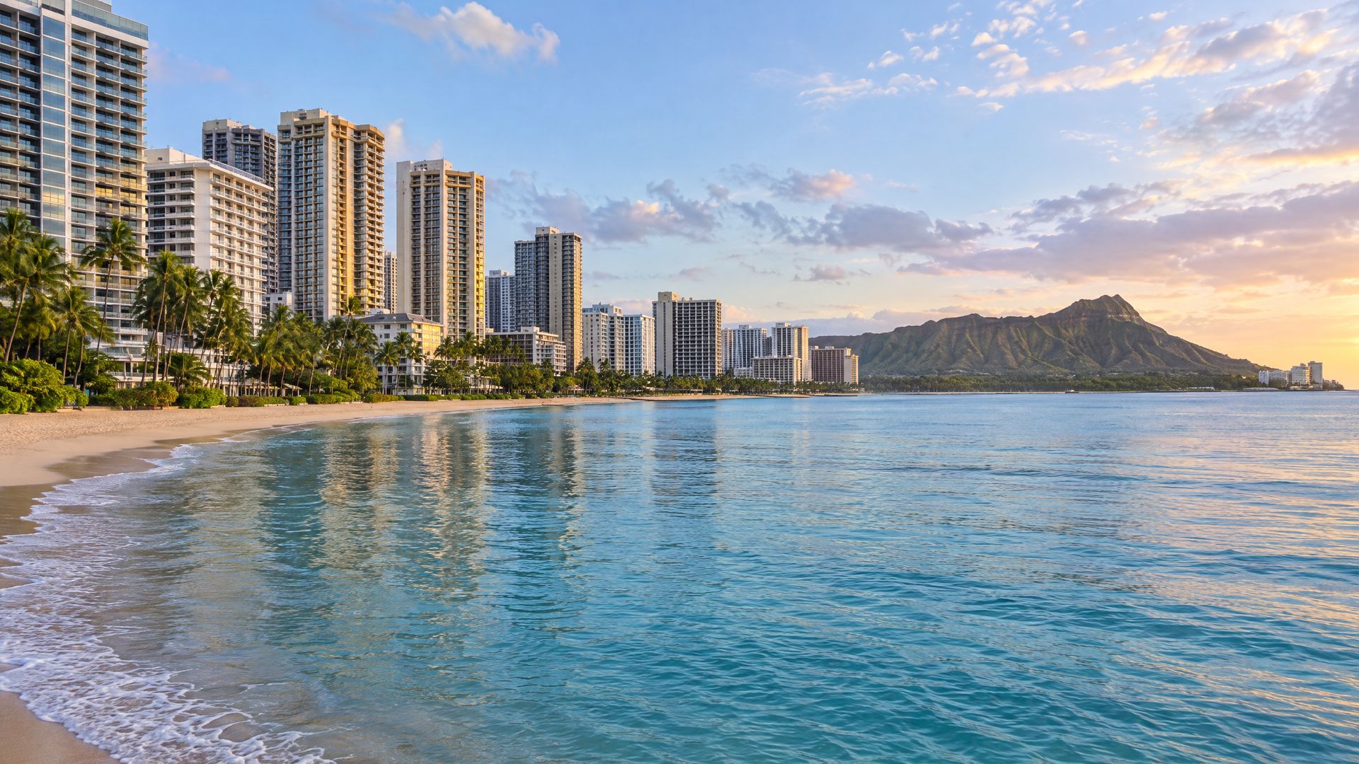 A curved sandy beach in Waikiki lined with high-rise towers and palms, with a crater headland at the far end.