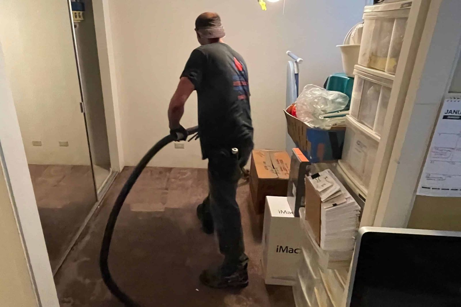 A Rescue One technician pulling standing water out of a carpeted room with an extraction hose.